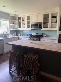 a kitchen with stainless steel appliances a sink dishwasher a stove a microwave oven and a dining table with wooden floor