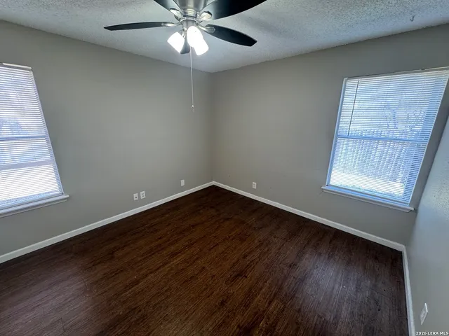 an empty room with wooden floor fan and windows