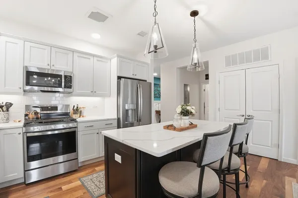 a kitchen with stainless steel appliances granite countertop a stove a refrigerator a kitchen island a dining table and chairs