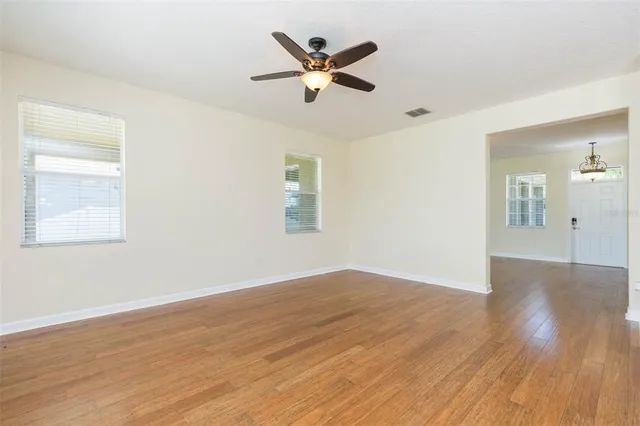 a view of an empty room with wooden floor and a ceiling fan