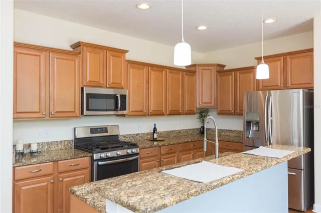 a kitchen with stainless steel appliances granite countertop a stove top oven a sink dishwasher and a refrigerator with wooden cabinets