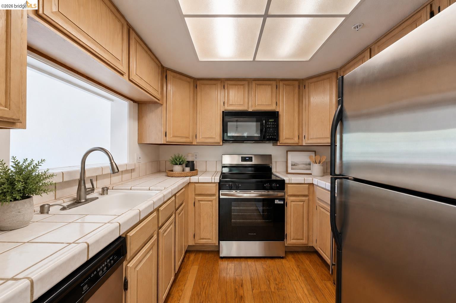 261 Redhawk Road Novato, CA 94949 - Photo 4 of 44 U-shaped kitchen featuring light wood cabinetry, tile countertops and backsplash, stainless steel appliances, and wood-finish flooring