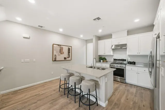 a kitchen with stainless steel appliances granite countertop a stove top oven a sink a refrigerator and white cabinets with wooden floor