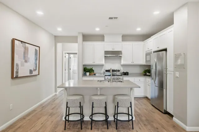 a kitchen with stainless steel appliances a refrigerator a stove a sink dishwasher and white cabinets with wooden floor