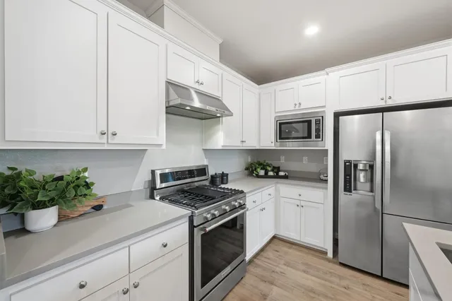 a kitchen with white cabinets stainless steel appliances and wooden floor