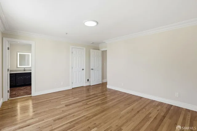 a view of a refrigerator in kitchen and an empty room with wooden floor