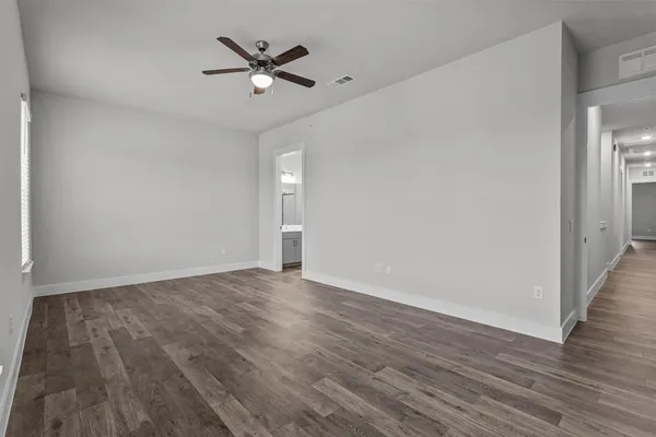 an empty room with wooden floor ceiling fan and windows