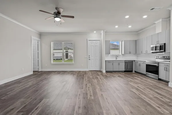 a view of an empty room with kitchen and window