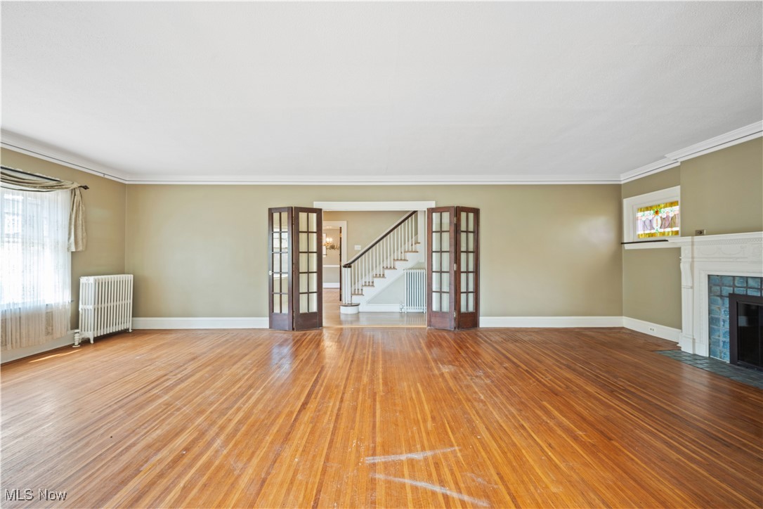 24510 Lake Road Bay Village, OH 44140 - Photo 14 of 45 Unfurnished living room featuring french doors, stairway, radiator heating unit, hardwood / wood-style flooring, and a tile fireplace