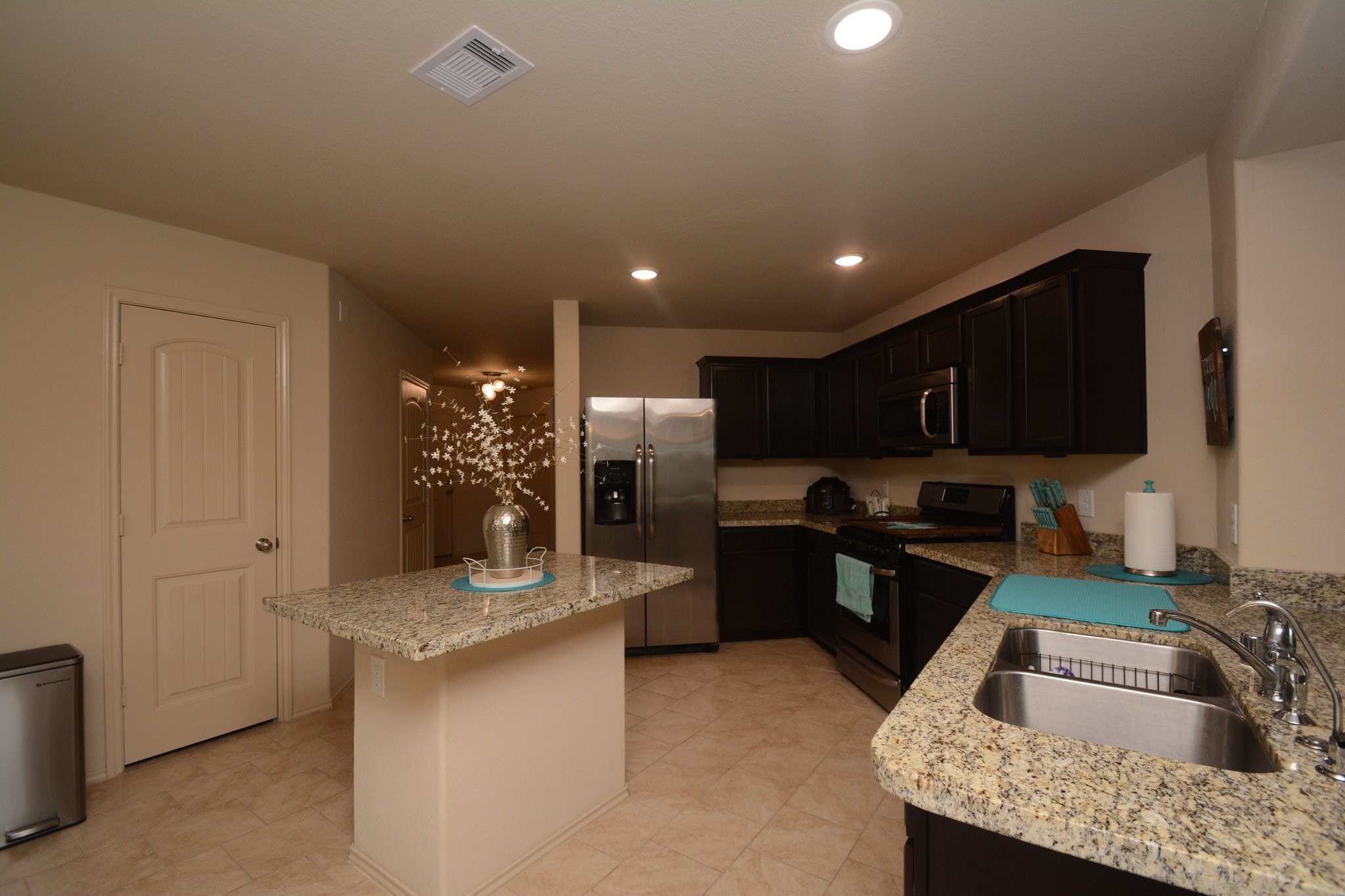 23318 Dukes Run Drive Spring, TX 77373 - Photo 7 of 41 This kitchen features dark wood cabinets, stainless steel appliances, and granite countertops. It includes a central island and a double sink, all set on light tile flooring, creating a modern and functional cooking space.