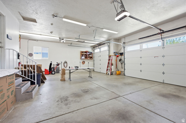 776 Flint Street Layton, UT 84041 - Photo 36 of 41 Spacious two-car garage featuring a concrete floor, multiple fluorescent light fixtures, two overhead garage doors with window panels, and a built-in shelving unit