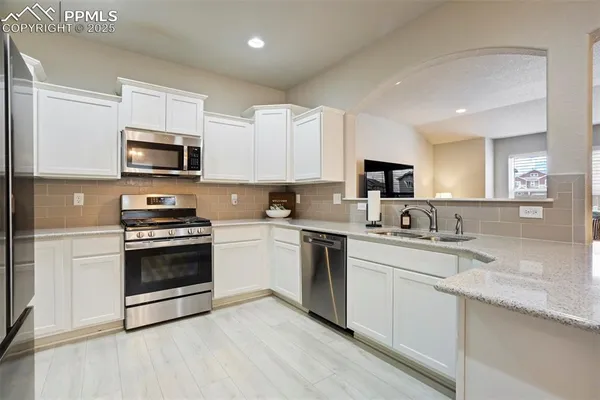 a kitchen with granite countertop a stove top oven a sink dishwasher a refrigerator and a microwave oven with wooden floor