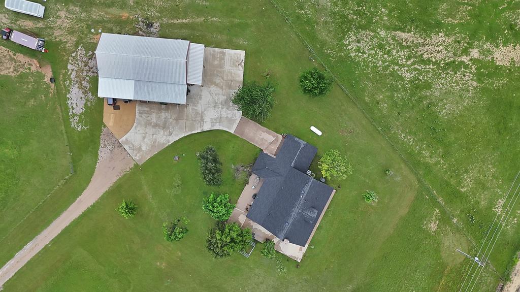 100 Shadle Ridge Court Poolville, TX 76487 - Photo 36 of 40 Expansive property featuring a primary residence with a dark shingled roof, a large metal-roofed outbuilding, and significant green space