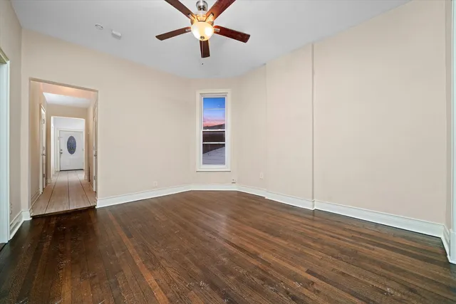 an empty room with wooden floor chandelier fan and windows