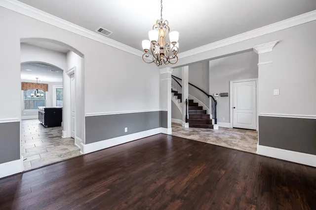 a view of an empty room with wooden floor staircase and a kitchen