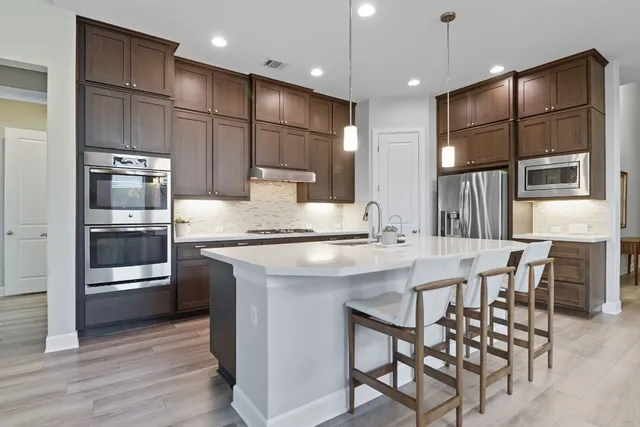 a kitchen with stainless steel appliances granite countertop a sink a stove a refrigerator and island with wooden floor