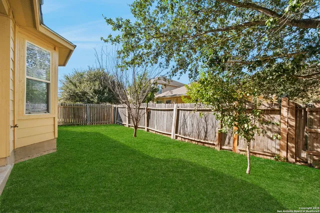 a view of a backyard with wooden fence and a large tree