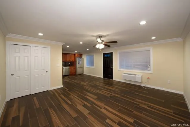 a view of an empty room with wooden floor and a kitchen
