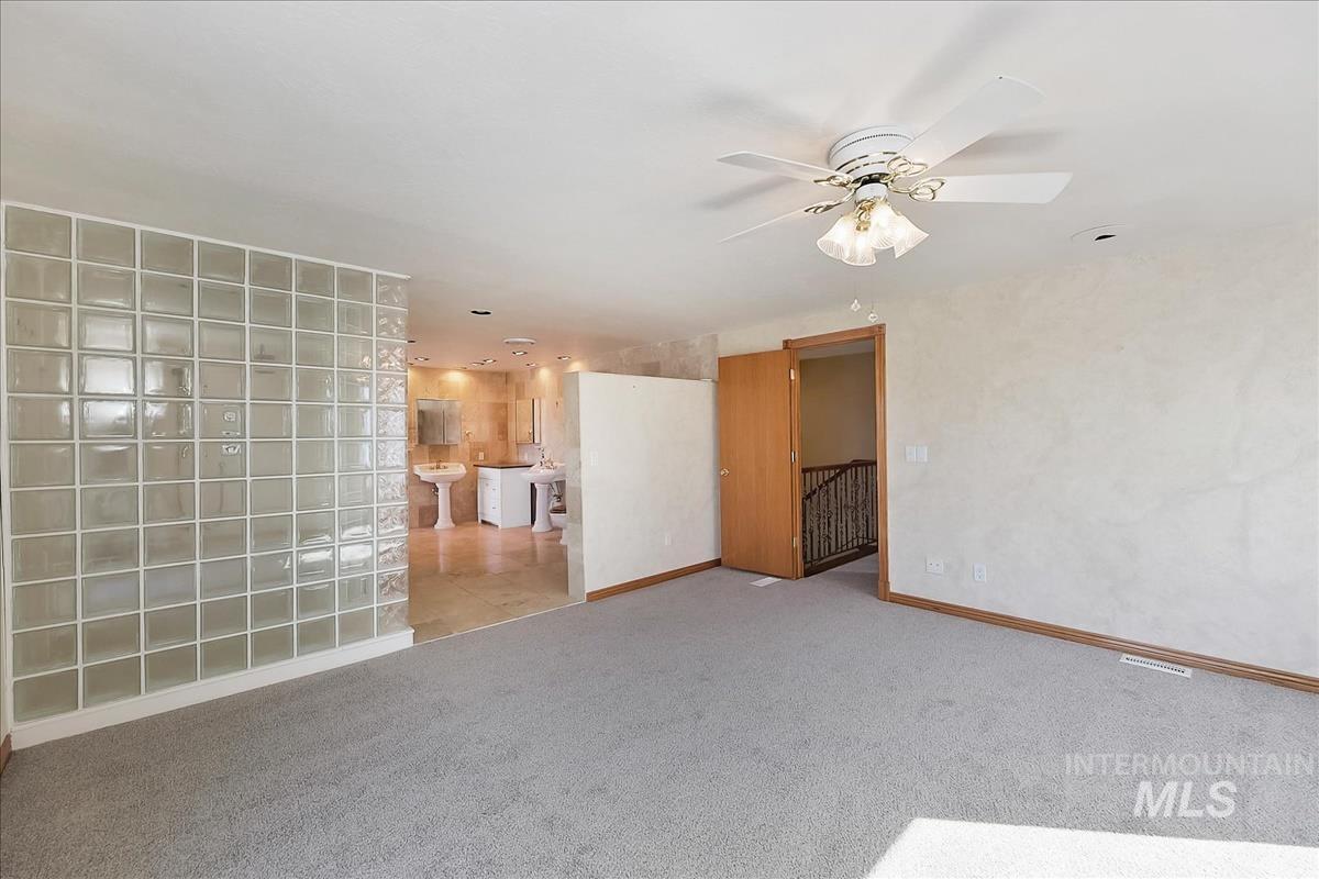 2804 West Sunrise Rim Road Boise, ID 83705 - Photo 37 of 50 Carpeted room featuring a glass block partition wall, a ceiling fan with integrated lighting, and a doorway opening to a staircase with a wrought iron railing