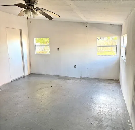an empty room with windows and chandelier fan