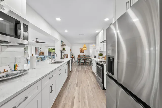 a kitchen with stainless steel appliances granite countertop a stove top oven a sink a refrigerator and white cabinets with wooden floor