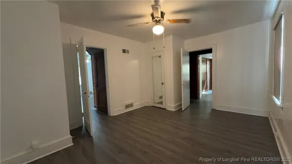 an empty room with wooden floor fan and windows