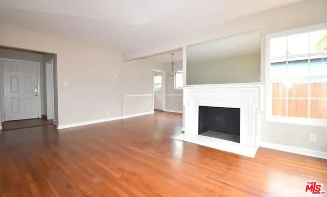 a view of an empty room with wooden floor fireplace and a window