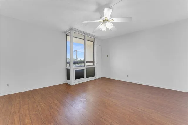 an empty room with wooden floor kitchen view and a ceiling fan