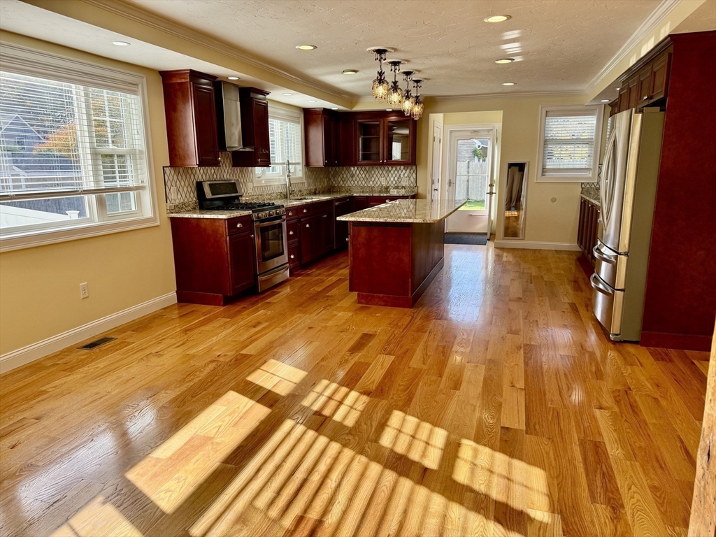 722 Lowell Street, Unit A Peabody, MA 01960 - Photo 10 of 40 a large kitchen with stainless steel appliances granite countertop a refrigerator a sink dishwasher a stove and a dining table with wooden floor