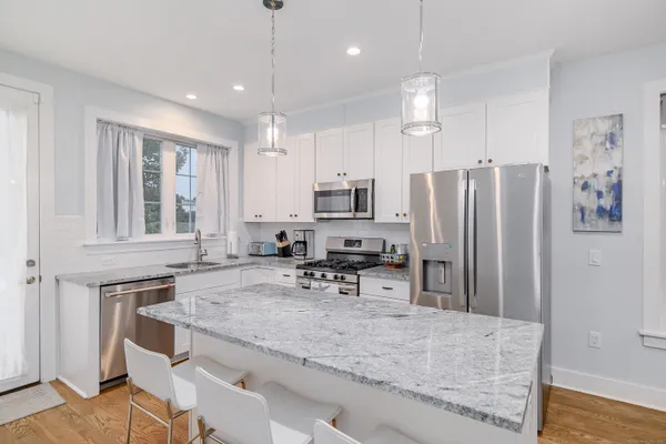 a kitchen with stainless steel appliances granite countertop a refrigerator a sink dishwasher a stove white cabinets and wooden floor