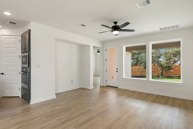 an empty room with wooden floor chandelier fan and windows