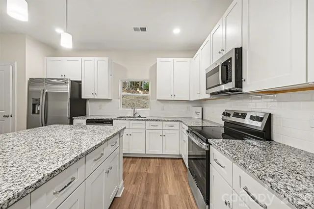 a kitchen with stainless steel appliances granite countertop a stove top oven a refrigerator a sink and dishwasher with wooden floor