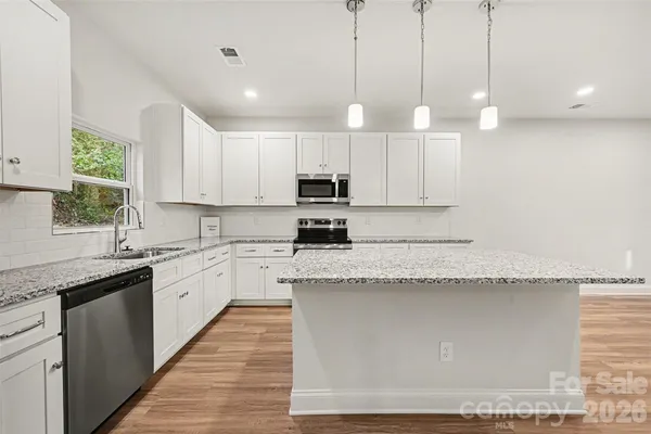 a large kitchen with granite countertop a sink a counter top space appliances and cabinets