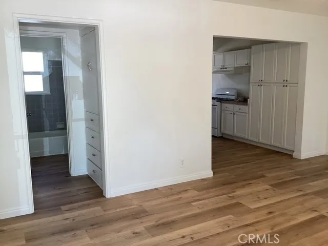 an empty room with wooden floor & kitchen space