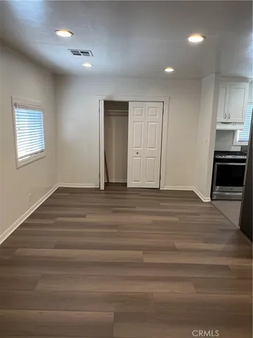 an empty room with wooden floor and kitchen view