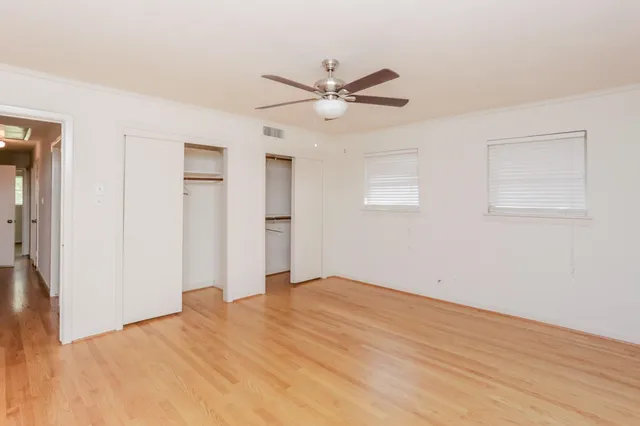 a view of an empty room with wooden floor and a ceiling fan