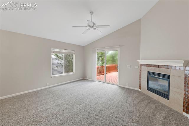 6725 Akron Road Colorado Springs, CO 80923 - Photo 18 of 50 Unfurnished living room featuring carpet, a tiled fireplace, lofted ceiling, and ceiling fan