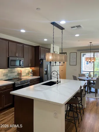 a kitchen with stainless steel appliances kitchen island granite countertop a dining table chairs refrigerator and microwave
