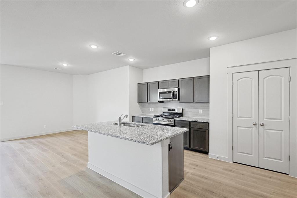 1759 Gleasondale Place Forney, TX 75126 - Photo 5 of 25 Kitchen with decorative backsplash, a center island with sink, stainless steel appliances, recessed lighting, and light stone countertops