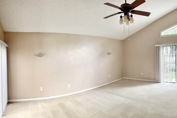 an empty room with chandelier fan and windows