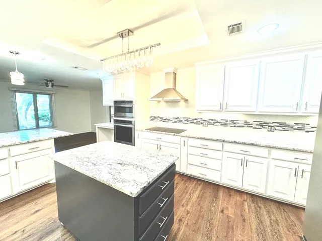 a kitchen with stainless steel appliances kitchen island granite countertop a sink stove and white cabinets with wooden floor