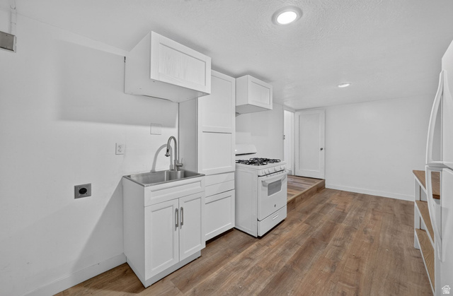 220 East Greenwood Avenue Midvale, UT 84047 - Photo 31 of 46 Compact kitchen area featuring wood-finish flooring, white cabinetry, a stainless steel utility sink with a high-arc faucet, a white gas range, and a white refrigerator
