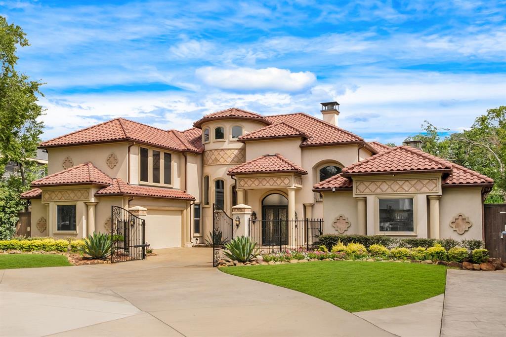 Stucco exterior residence featuring a red tile roof, arched entryways, decorative iron gates, an attached garage, and a concrete driveway