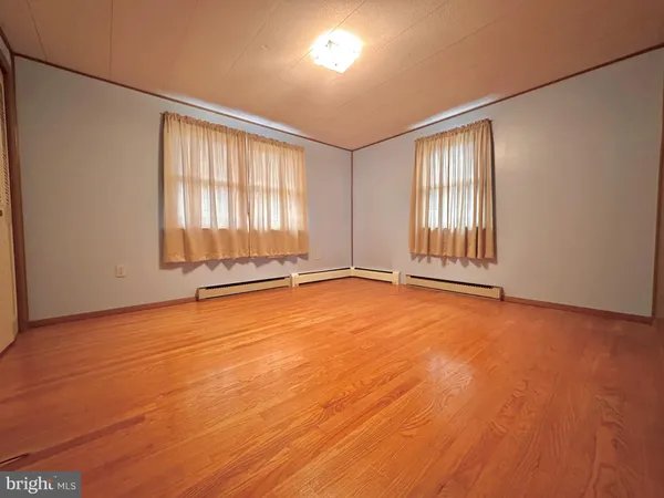 an empty room with wooden floor and windows with curtains