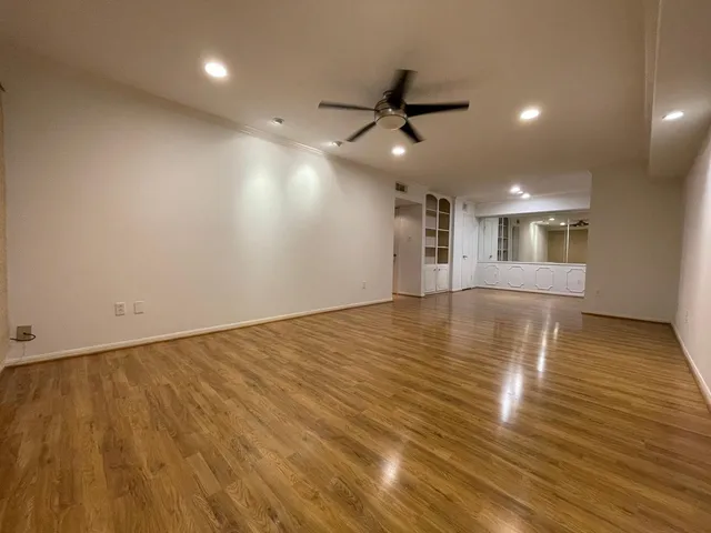 an empty room with wooden floor a ceiling fan and kitchen view
