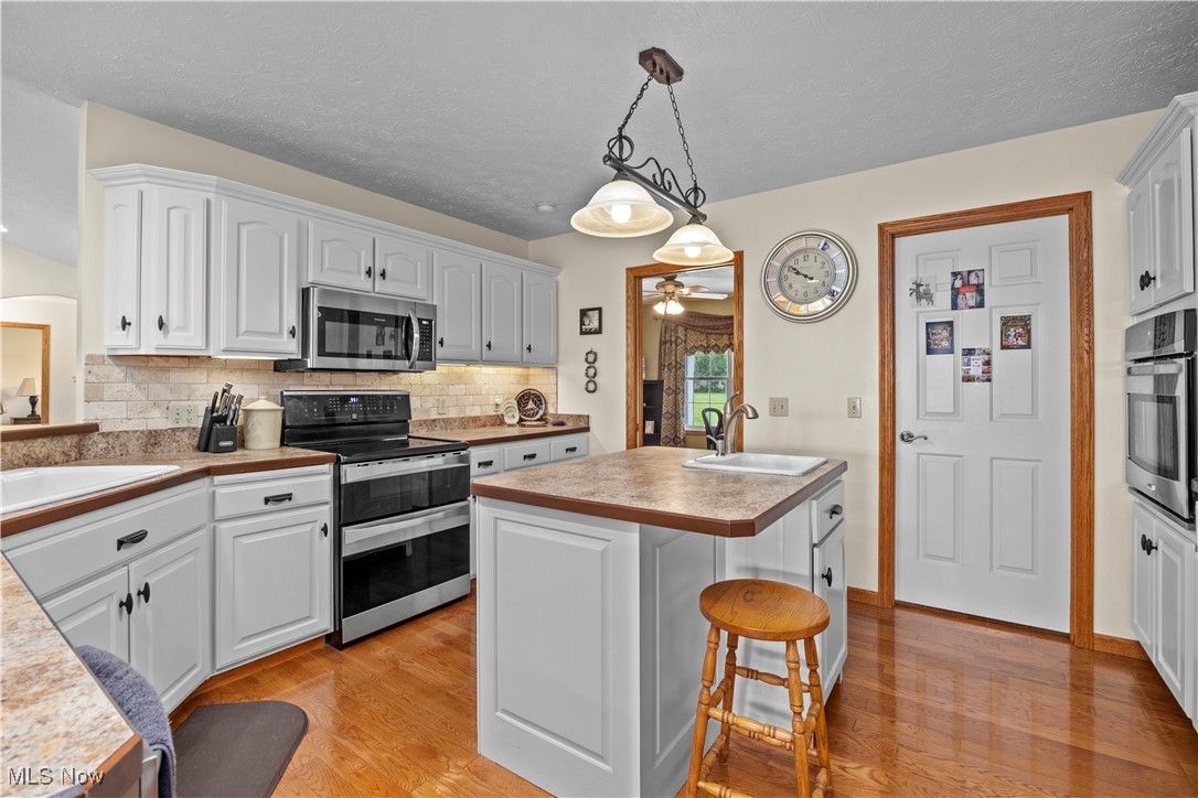 47147 Merriam Road Wellington, OH 44090 - Photo 20 of 49 Kitchen featuring appliances with stainless steel finishes, light wood flooring, a ceiling fan, tasteful backsplash, and a kitchen breakfast bar