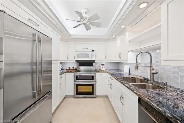 a kitchen with stainless steel appliances granite countertop a sink a stove a refrigerator cabinets and a window