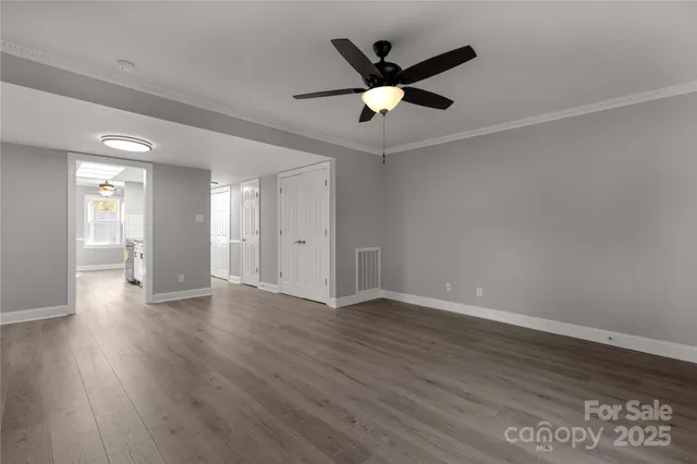 a view of an empty room with wooden floor and a ceiling fan
