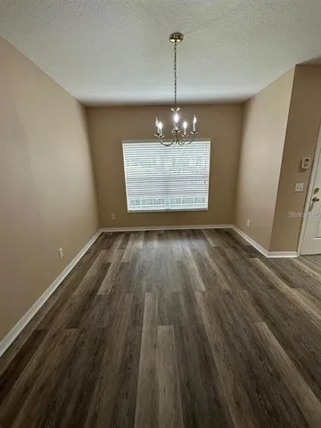a view of empty room with wooden floor chandelier and window