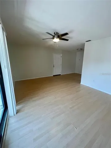 an empty room with wooden floor fan and windows